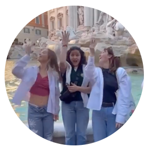 Three students throw coins over their shoulder into a fountain